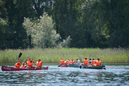 Kinder-fahren-mit-schwimmweste-am-schilf-des-seeufers-entlang