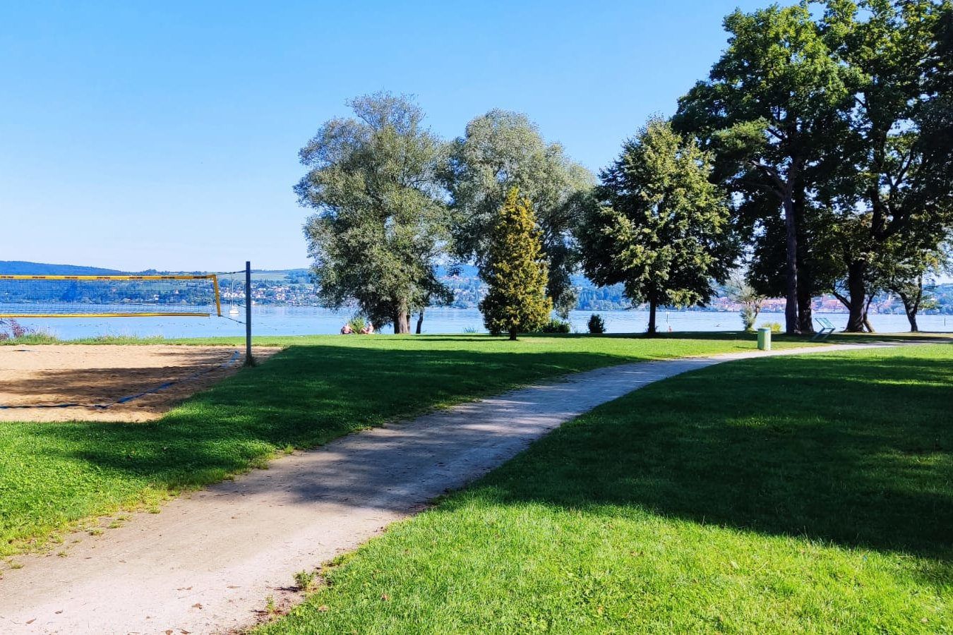 Blick-auf-die-wiese-im-strandbad-mit-schatten-der-baeume-und-see-im-hintergrund