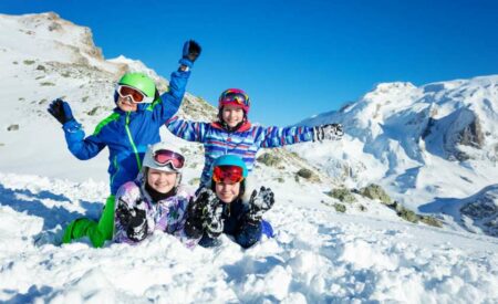 vier-kinder-sitzen-im-schnee-beim-ski-fahren