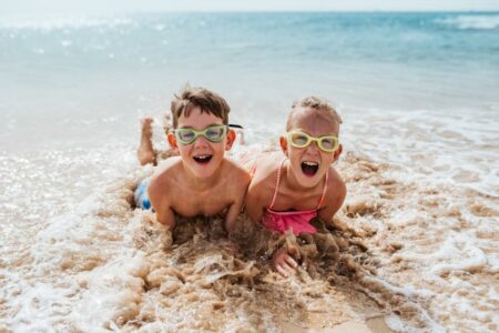 zwei-kinder-liegen-im-meer-und-lachen