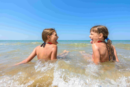 zwei-maedchen-sitzen-im-meer-die-zunge-rausstreckend